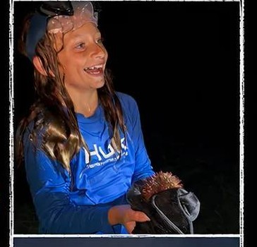 A young guest smiling and holding a sea urchin found during a guided night tour.